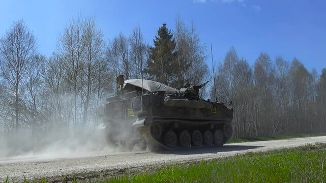 Rare awesome military footage of a FV432 armoured vehilve with infanrty on it driving by on a dusty white countryside road in a ummer sunny forest during an battle exercise called SIIL 2025, slow-mo.