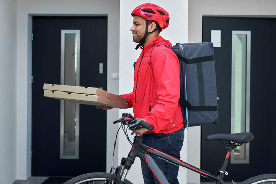 Delivery person with pizza boxes and bicycle standing at house