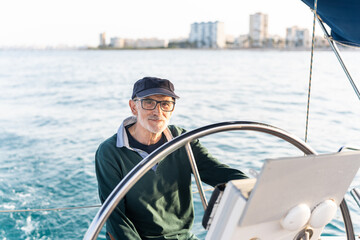 Senior skipper steering sailboat on sunny day in ocean