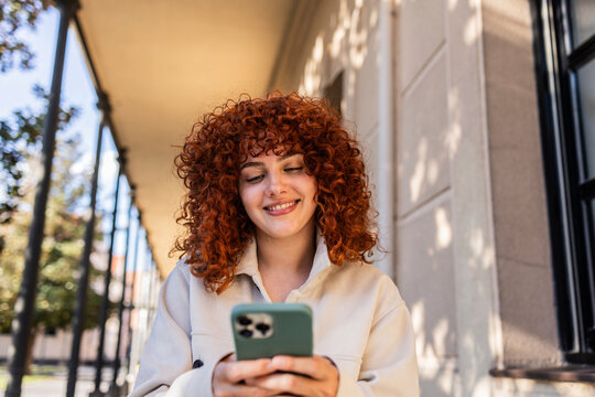 Student with curly red hair using smartphone on university campus