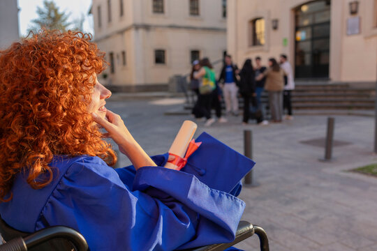 Young woman with red curly hair in a wheelchair at a graduation ceremony outdoors