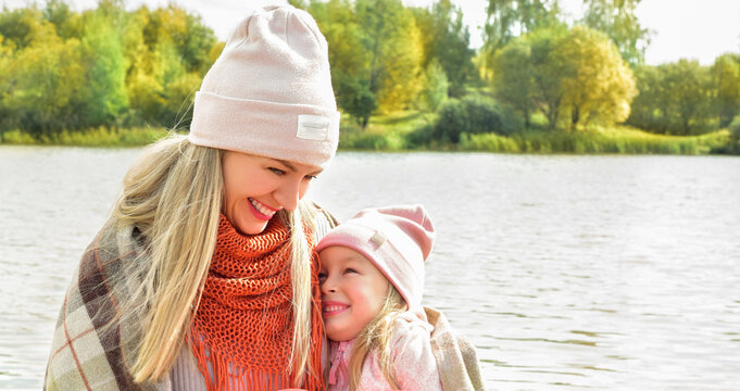 Mom and daughter on a bench. Mother and daughter on a walk. Autumn season. Sunny day. Happy family outdoors