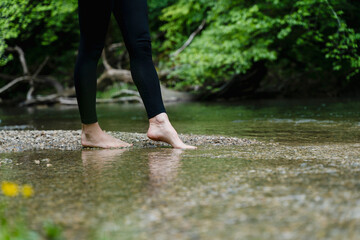 Bare feet stepping into a stream in a green forest promoting holistic health and mental well-being
