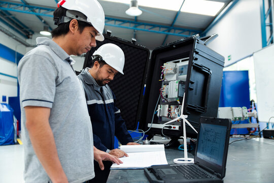 Engineers in a workshop inspecting electrical equipment with a laptop and control panel