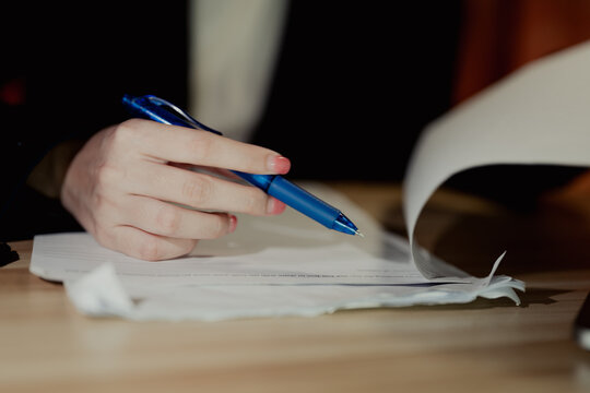 A businesswoman flipping through papers while holding a pen, representing review or approval process in an office.