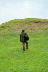 A male adventurer is enjoying the beauty of the expanse of green grass. The Asian male traveler relaxes and is amazed by the natural charm of the clean and beautiful green hills.