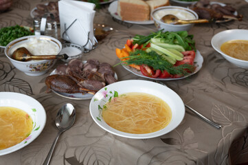 Festive table setting with traditional dishes including chicken noodle soup, smoked goose, and fresh salad