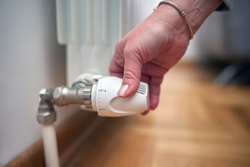 Plakat Woman rotating heating valve on a chilly winter day, energy and gas crisis, cold room, heating problems.