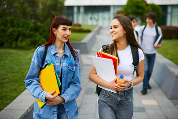 Two female university students walking and chatting together on campus between classes