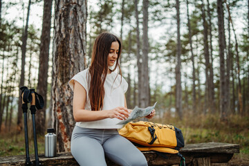 Young woman take a break after hike or trek to look at map and drink water 
