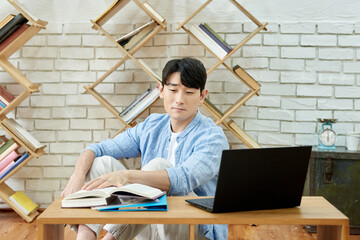 Young Asian Man Studying with Laptop and Books in Bright Modern Home Office