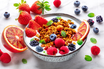Granola with yogurt and fresh fruit. Organic gourmet muesli on a marble table with ingredients. Strawberry, orange, and mint