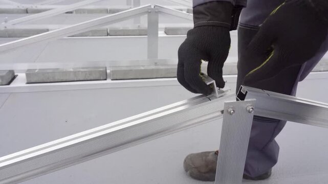 A worker prepares an aluminum frame for mounting and installing solar panels.
