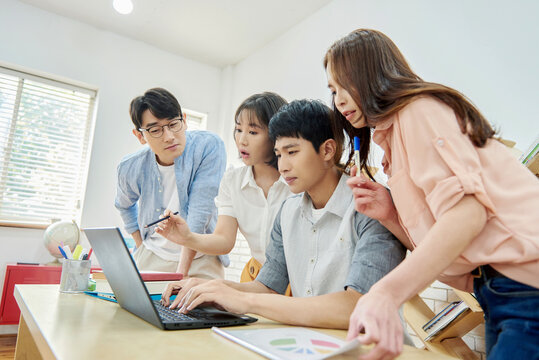 Young Asian Men and Women Collaborating on Project Around Laptop in Modern Study Room