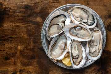 Fresh raw oysters on ice, overhead flat lay shot on a rustic wooden table, with lemon, with a place for text