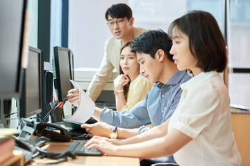 Young Asian Man and Woman Working Together in Modern Office with Computers and Telephone