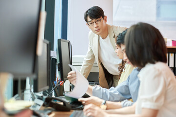 Fototapeta premium Young Asian Man and Woman Working Together in Modern Office with Computers and Telephone