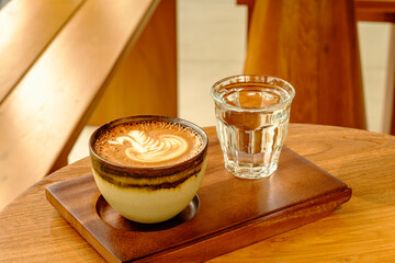 Latte Art Coffee with Glass of Water on Wooden Tray in Cafe