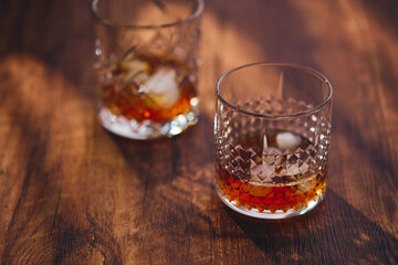 Glasses of whiskey with ice and lemon slices on a wooden table in the rays of light. Shallow depth of field
