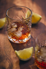 Glasses of whiskey with ice and lemon slices on a wooden table in the rays of light. Shallow depth of field