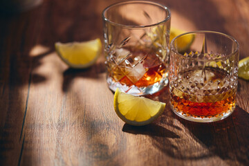 Glasses of whiskey with ice and lemon slices on a wooden table in the rays of light. Shallow depth of field