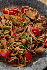 Wok with Soba noodles with turkey, mushrooms and sweet red bell pepper in plate on wooden table in the sun. Asian food, concept of street food. Top view. Close up.