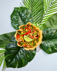 Fajitas in tortilla bowl with beef, cheese, corn and lettuce on faux monstera leaf