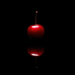 Obraz premium Bright red cherry on black reflective surface