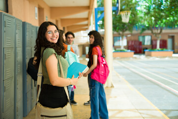Portrait of smiling high school student girl holding books in school hallway
