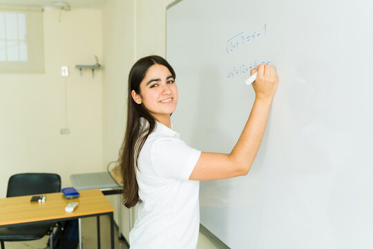 Smiling high school student solving math equations on whiteboard