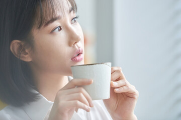 Young Asian Woman Enjoying a Cup of Coffee Indoors by the Window in the Morning