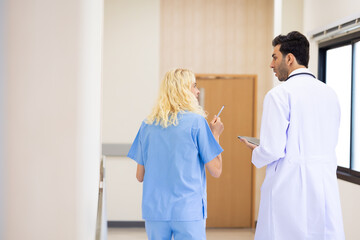 Obraz premium Back view : Multi-ethnic healthcare workers in hospital. nurse and doctor walking in corridor and talking and in discussion for advice, medical service, diagnosis and consulting
