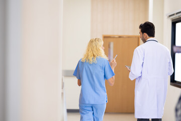 Fototapeta premium Back view : Multi-ethnic healthcare workers in hospital. nurse and doctor walking in corridor and talking and in discussion for advice, medical service, diagnosis and consulting