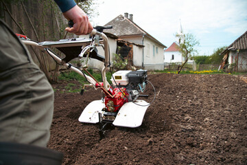 Organic farming man cultivates the ground with a tiller preparing the soil for sowing