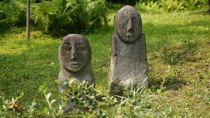 Ancient-style stone statues in a peaceful green garden, surrounded by ferns and grass—perfect for...