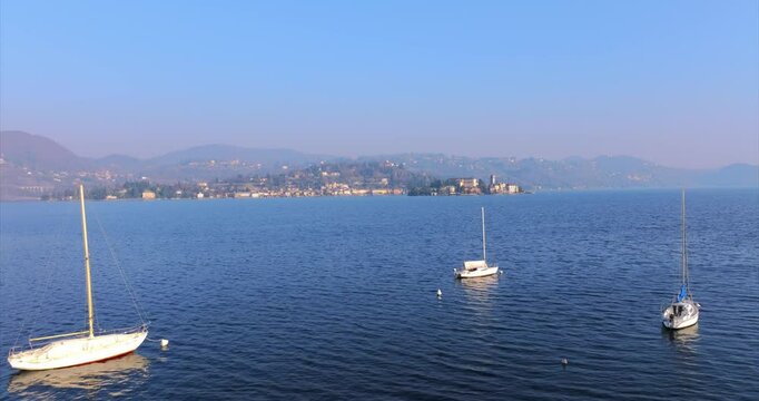Sailboats Floating On Calm Waters Of Lake Orta In Pella, Piedmont, Italy. ascending drone shot