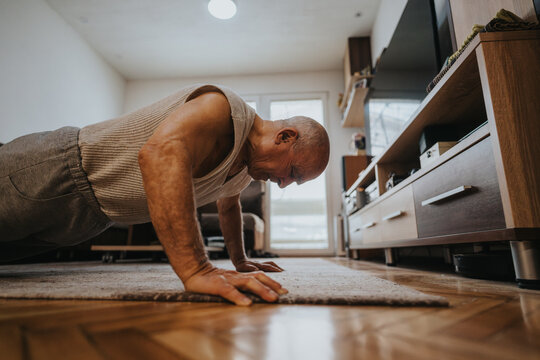 Elderly man exercising by performing push-ups on a rug in a stylish, modern living room, symbolizing active aging and commitment to physical health.