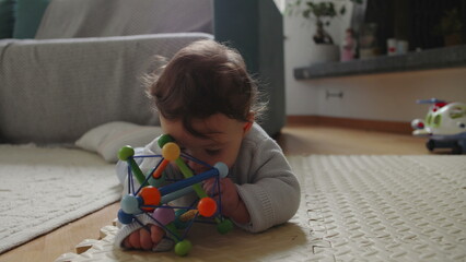 Baby playing with colorful toy on mat, developing motor skills through tactile exploration and...