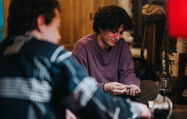 Two friends are spending time together indoors, sharing drinks and enjoying a friendly conversation in a cozy setting. The ambiance features warm lighting and a relaxed mood, promoting a close bond.