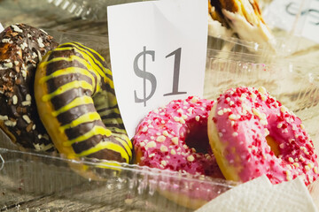 Donuts with glaze in a clear plastic container with a price tag of $1 for sale, close-up, price on...