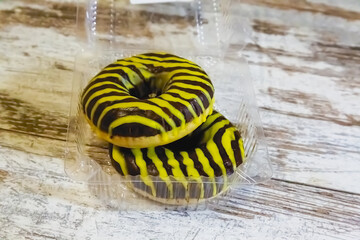 Two chocolate donuts in a clear plastic container on a white wooden table close-up.