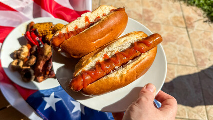 Hand grasps sizzling hot dogs drenched in zesty ketchup, evoking sunlit Americana, Fourth of July BBQ, savory indulgence