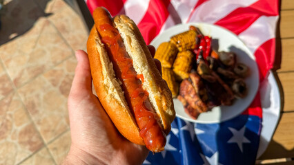A robust grip on ketchup-slathered hot dog, sizzling American cookout vibes, Independence Day feast, backyard barbecue, culinary Americana