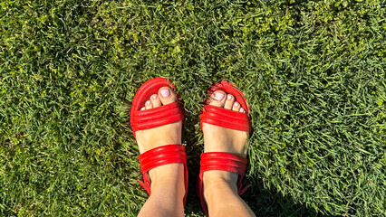 Vibrant red sandals on verdant grass, evoking Midsummer revelry, barefoot grounding, nostalgic childhood playgrounds, female, carefree spirit