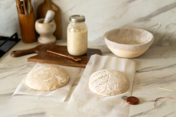 Freshly prepared sourdough bread dough rests on parchment near a container of active starter and a mixing bowl, showcasing the art of home baking.