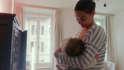 Mother breastfeeding her baby while standing in the bedroom, comforting and nurturing, intimate...