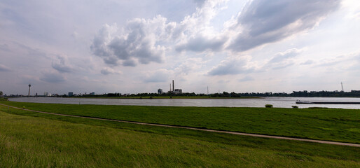 Fototapeta premium Grass field, Rhine river and Dusseldorf in the distance with cloudy sky
