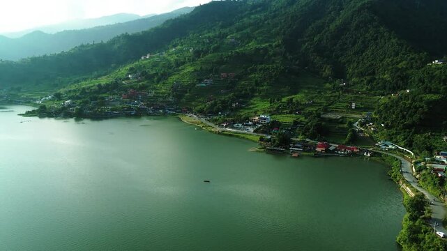A tranquil lakeside village nestled against lush green hills, with scattered houses and a calm turquoise lake.