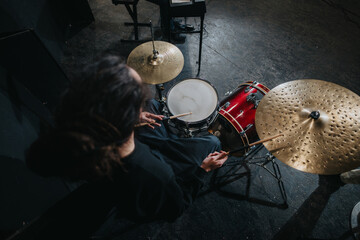 A musician seated at a drum set performs in a dimly lit studio environment. Great for themes of...