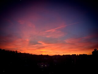 A view of the early evening red-tinged sky just after sunset. The silhouette of the city houses is visible.